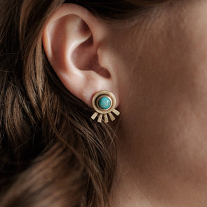 Close-up of an ear wearing a gold earring with a turquoise stone.