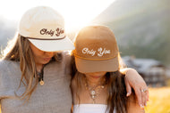 Two people wearing hats with 'Only You' text, standing close together outdoors.