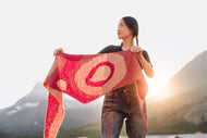 Person holding a red and pink patterned fabric against a mountainous background