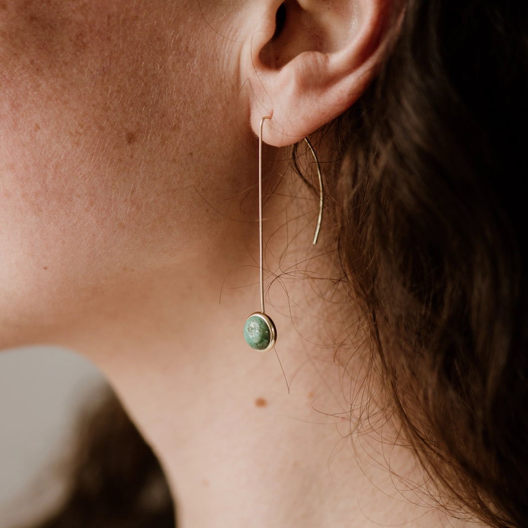 Close-up of an ear wearing a green stone earring with a blurred background