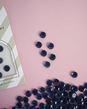 Load image into Gallery viewer, Blue buttons scattered on a pink surface with a box labeled 'Buttons' in the corner.