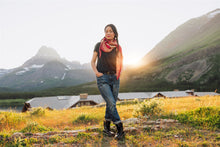 Load image into Gallery viewer, Woman standing in a scenic outdoor setting with mountains and a building in the background.