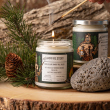 Load image into Gallery viewer, Candle labeled &#39;A Campfire Story&#39; being lit with a match, surrounded by natural elements on a wooden surface.
