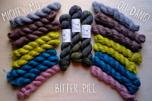 Load image into Gallery viewer, Colorful yarn skeins labeled 'Mighty Mo', 'Oh Dang!', and 'Bitter Pill' on a wooden surface.