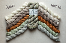 Load image into Gallery viewer, Skeins of twisted yarn arranged in a fan shape on a light beige fabric background, with two small labels in the center. The yarn colors include cream, taupe, orange, sage green, and light gray.