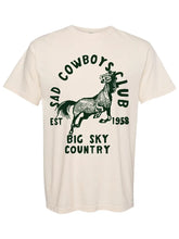 Load image into Gallery viewer, An off-white short-sleeve t-shirt with a dark green graphic print featuring a cowboy horse and the text 'Sad Cowboys Club', 'Big Sky Country', and 'Est. 1958'.