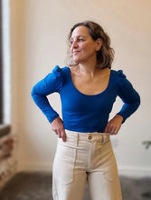 Load image into Gallery viewer, Woman wearing a blue top and beige pants against a neutral background
