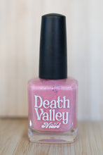 Load image into Gallery viewer, Pink nail polish bottle with black cap on a wooden surface