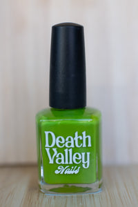 Green nail polish bottle with black cap on a wooden surface