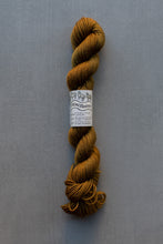 Load image into Gallery viewer, A skein of mustard yellow yarn with a white paper label reading 'Mini skeins' and 'Sandy Gold', photographed vertically against a textured gray background.