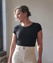 Load image into Gallery viewer, Woman wearing a black t-shirt and beige pants standing against a neutral wall.