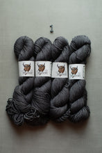 Load image into Gallery viewer, Four skeins of dark charcoal gray yarn arranged side by side on a light gray textured background, with a small number 1 printed above them. Each skein has a white paper label featuring a brown buffalo illustration.