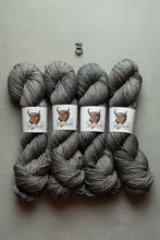 Load image into Gallery viewer, Four skeins of heather gray yarn arranged in two rows on a light gray background, with a small metal number 3 above them. Each skein has a white paper label featuring a brown bison illustration and the brand name Prairie Wind.