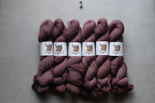 Load image into Gallery viewer, skeins of dusty mauve yarn arranged in a fan shape on a light gray background, each wrapped with a white paper label featuring a brown horned animal illustration.