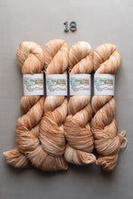 Load image into Gallery viewer, Four skeins of variegated yarn arranged in a row on a gray background, with a small metal '18' above them. The yarn is labeled 'Great Falls Cream' by the brand Great Falls Yarn Co.