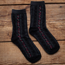 Load image into Gallery viewer, Black socks with red and green patterns on a wooden surface