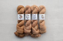 Load image into Gallery viewer, Four skeins of brown yarn on a gray background with labels.