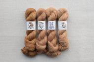 Four skeins of brown yarn on a gray background with labels.