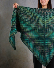 Load image into Gallery viewer, Person holding up a green and black patterned knitted shawl against a gray background