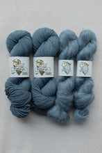 Load image into Gallery viewer, Four skeins of Piskun 'Pumpkin' yarn in a dusty slate blue-gray color, arranged side-by-side on a light beige textured fabric background.