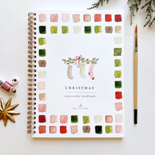 Load image into Gallery viewer, Christmas watercolor workbook with colorful swatches and a pen on a white background