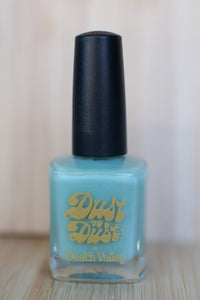 Nail polish bottle with black cap and blue liquid, featuring 'Dust to Dust' branding.