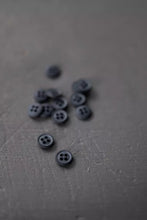 Load image into Gallery viewer, Black buttons scattered on a textured gray surface