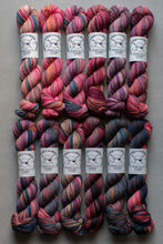 Load image into Gallery viewer, Six skeins of variegated yarn arranged in two rows on a gray background. Each skein has a white paper label wrapped around it with a black skull-and-crossbones logo and the text 'Capricelli Yarn'.