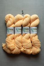 Load image into Gallery viewer, Four skeins of soft peach-colored yarn arranged side by side on a gray background, each with a paper label reading 'Great Falls Yarn Co.' A small metal '1' is placed above the yarn.