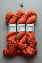 Load image into Gallery viewer, Three skeins of Great Falls Rock Mountain yarn in a warm orange color, arranged vertically on a gray background with a small black number 4 above them.