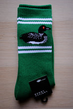 Load image into Gallery viewer, A single green knit sock with white stripes and a black-and-white loon graphic, shown folded on a light wood surface with a black brand tag attached.
