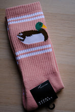 Load image into Gallery viewer, A pair of dusty pink ribbed socks with white stripes and a pixelated duck design, shown on a light wood background with a black brand tag.