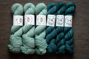 Six skeins of teal yarn with labels on a dark surface