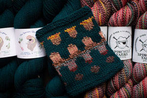 Knitted swatch with fox pattern surrounded by Spincycle Yarns yarn balls