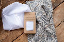 Load image into Gallery viewer, Cocoknits sweater care washing bag packaging on a wooden surface with a patterned sweater.