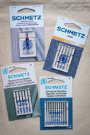 Four packages of Schmetz needles on a wooden surface