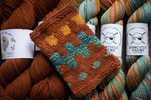 Load image into Gallery viewer, Knitted swatch with pattern on yarn balls labeled &#39;Spincycle Yarns&#39;.