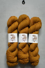 Load image into Gallery viewer, Three skeins of mustard yellow yarn with labels on a gray background