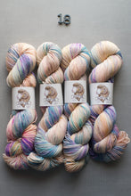 Load image into Gallery viewer, Four skeins of multicolored yarn on a gray background with a brand label.