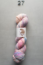 Load image into Gallery viewer, Multicolored skein of yarn with a label on a gray background