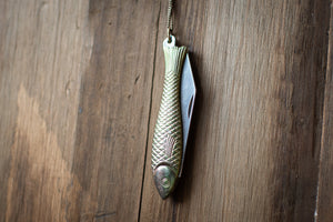 Fishing lure shaped like a fish with a pocket knife on a wooden surface