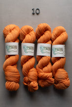 Load image into Gallery viewer, Four skeins of orange yarn with labels on a gray background