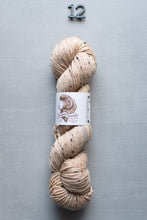 Load image into Gallery viewer, Beige skein of yarn with a label on a gray background