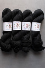 Load image into Gallery viewer, Four skeins of black yarn with labels on a gray background