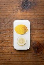 Load image into Gallery viewer, Two lemons, whole and sliced, on a white rectangular plate on a wooden surface.