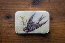Load image into Gallery viewer, Metallic tin with a bird illustration on a wooden surface