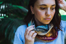 Load image into Gallery viewer, A woman wearing a colorful, patterned knit cowl scarf in a natural outdoor setting with green foliage in the background.