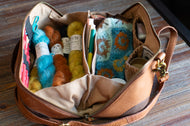Brown leather bag with colorful yarn and knitting supplies on a wooden surface