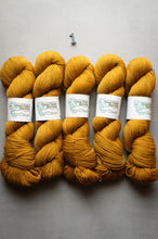 Load image into Gallery viewer, Six skeins of mustard yellow yarn with labels on a gray background