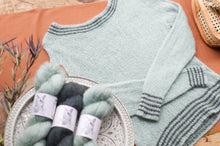 Load image into Gallery viewer, Light blue knitted sweater with yarn on a wooden surface